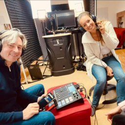 Zwei Personen in einem Aufnahmestudio, lächelnd, mit Kopfhörern und Equipment.